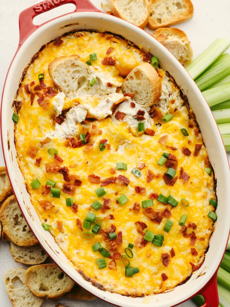 Crack chicken dip baked in a pan and being dipped with bread. 