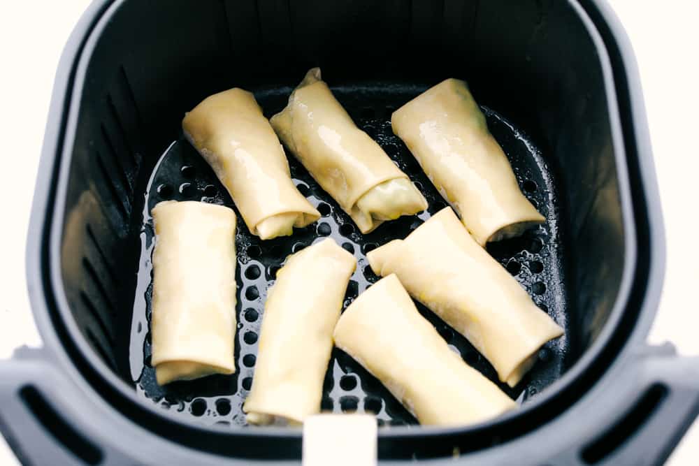 Air fryer basket filled with avocado egg rolls for frying.