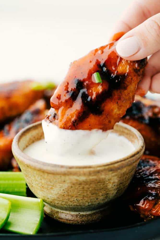 Dipping a chicken wing into white sauce.