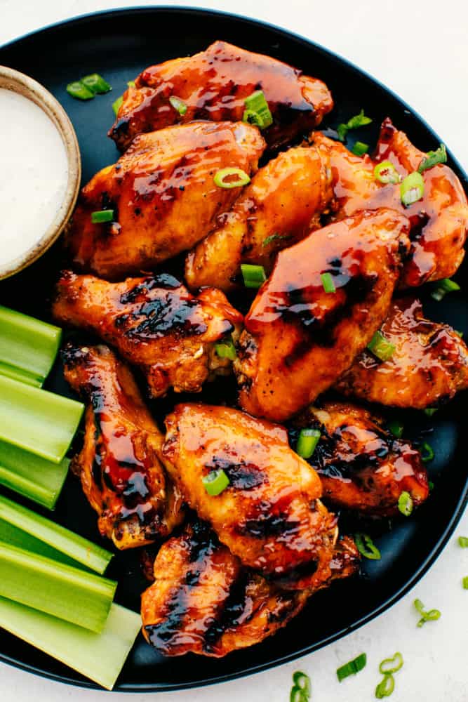 Grilled Honey Buffalo Wings on a black plate with celery and white dip.